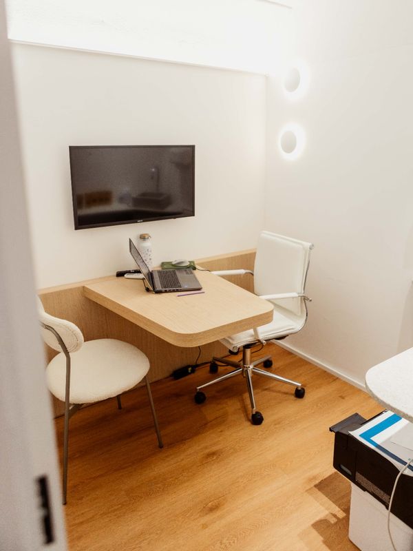 Consultório médico com mesa, cadeiras e tela na parede